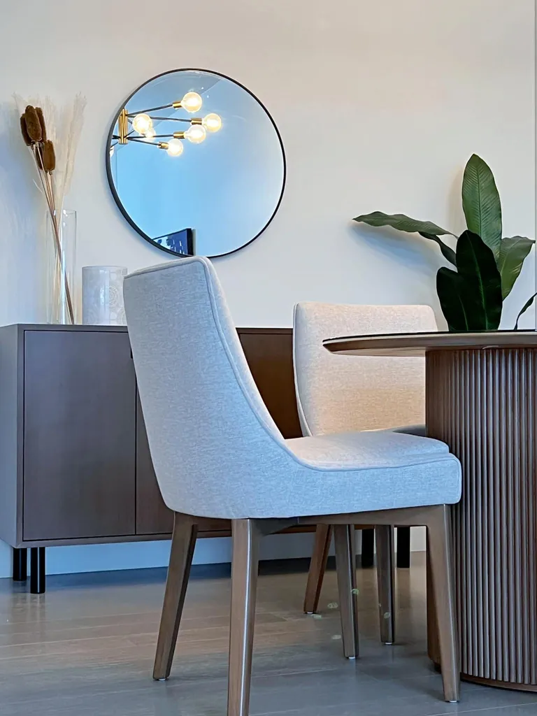 Grey upholstered dining chairs at a fluted round table, with a walnut sideboard behind
