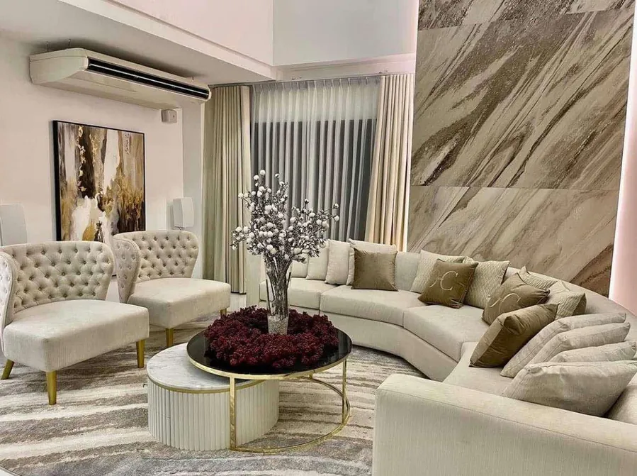 Cream curved sectional sofa with two button-tufted lounge chairs around a brass-framed coffee table